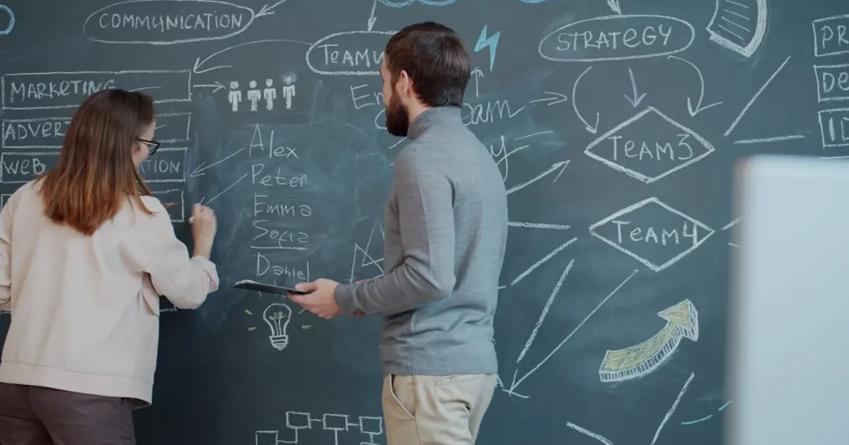 Two people planning on a chalkboard with diagrams.