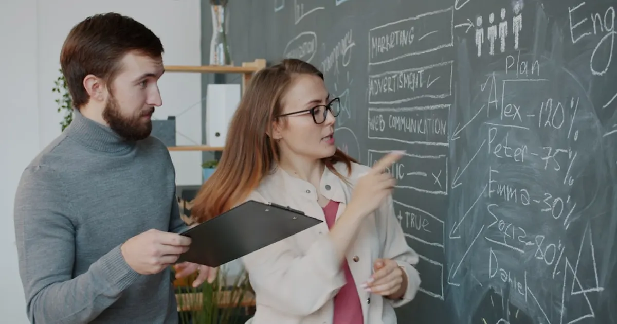 Two colleagues discussing a diagram on a chalkboard.